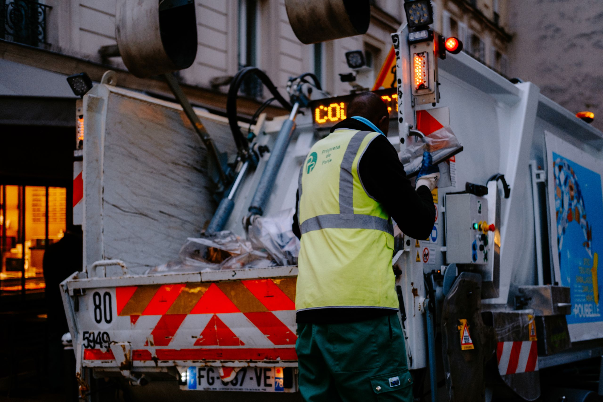 A garbage collector works on a city street, managing waste collection at dusk.